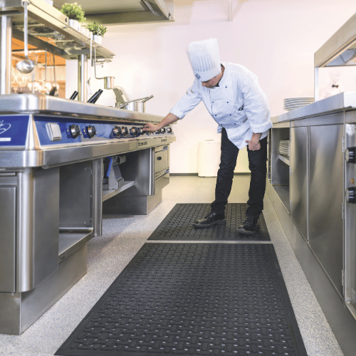 Chef working at a commercial kitchen range while standing on black Anti-Microbial Comfort Rubber Mats with drainage holes