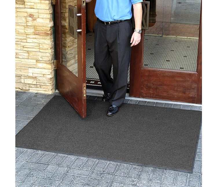 Man in a blue shirt stepping out through a wooden door onto a grey Brush Hog outdoor entrance mat on block paving